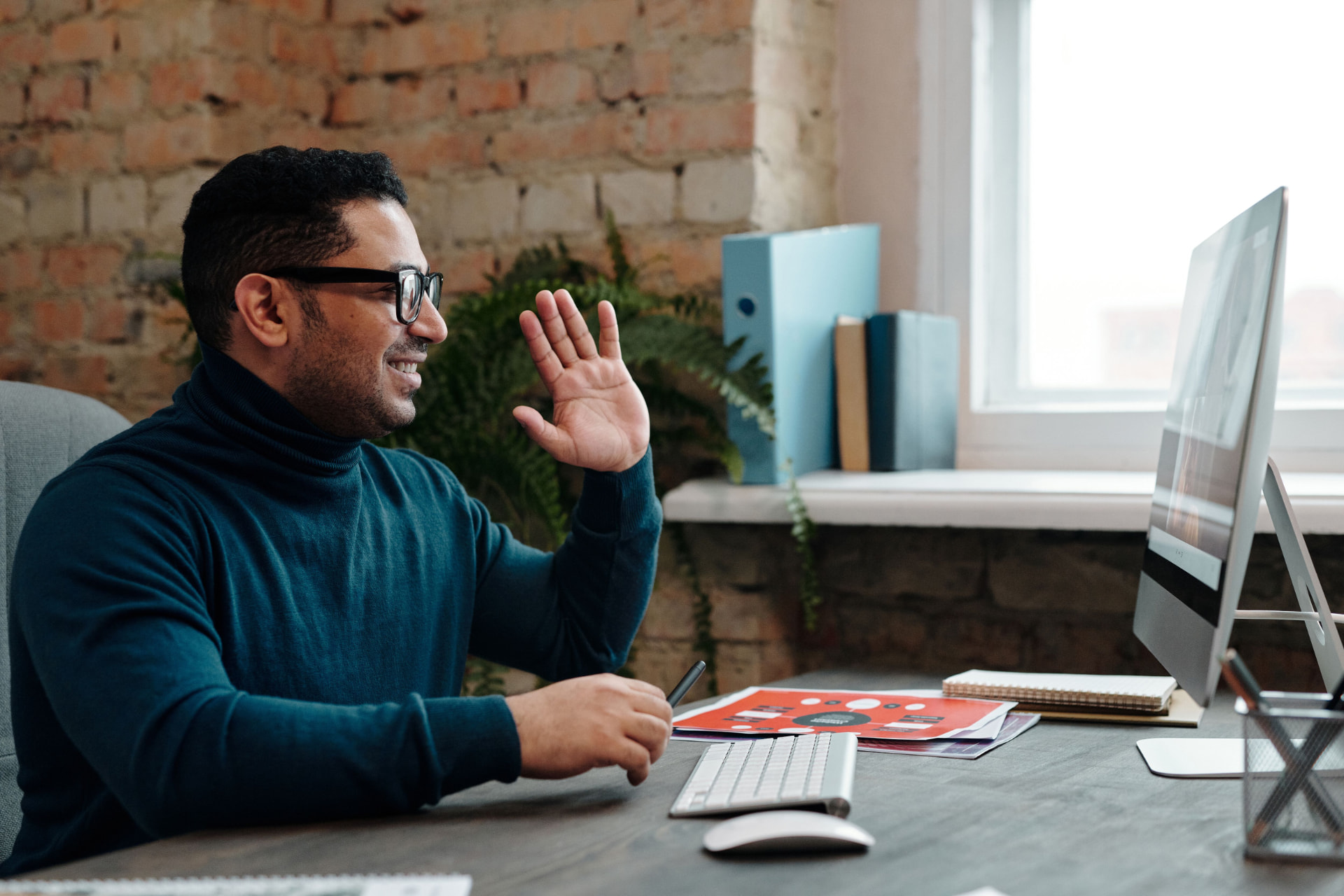 An employee waving during a virtual healthcare visit at his desk