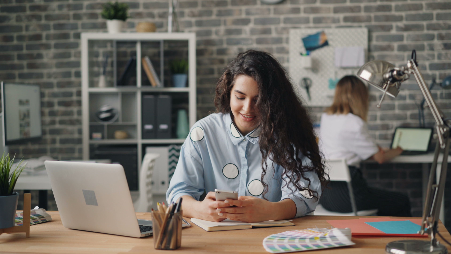An employee smiling while using her phone at her office desk